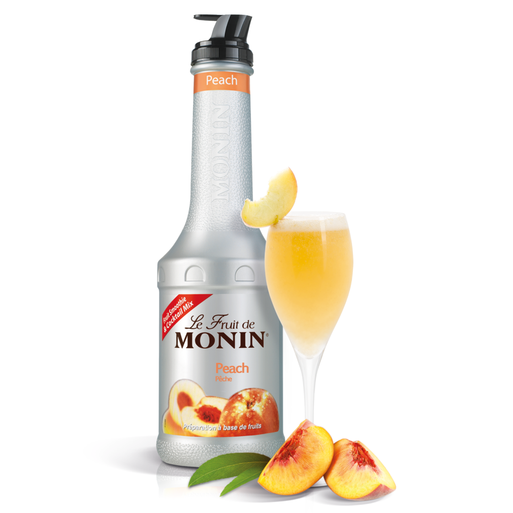 A bottle of Le Fruit de Monin Peach syrup stands next to a filled champagne flute with peach slices on a white background, with additional peach slices and green leaves at the base.