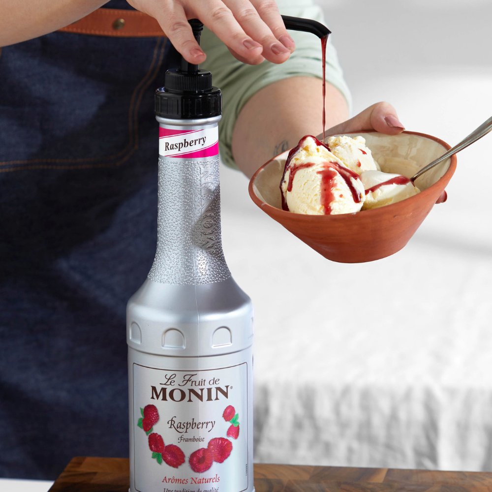 Monin Raspberry Puree 1 Ltr Bottle. Monin raspberry puree bottle with a person pouring it over ice cream in a Bowl - Discount Coffee