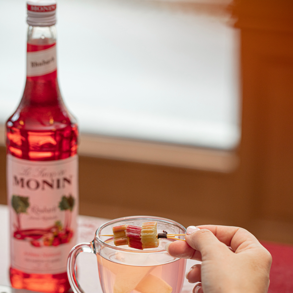 Monin Rhubarb Syrup (700ml) A Glass of Hot Rhubarb Drink With a Hand - Discount Coffee